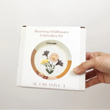 Hand holding an embroidery kit packaging with floral design on a white background